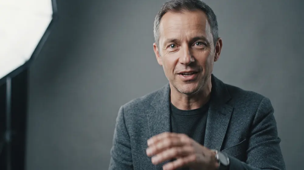 A close portrait of a presenter lit by a large softbox, catchlights visible in the eyes, plain grey backdrop behind