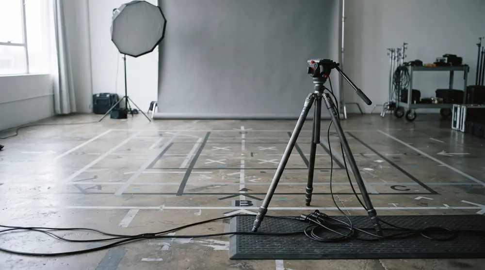 An empty studio floor marked out with gaffer tape in front of a plain grey backdrop, a tripod standing just outside the marks