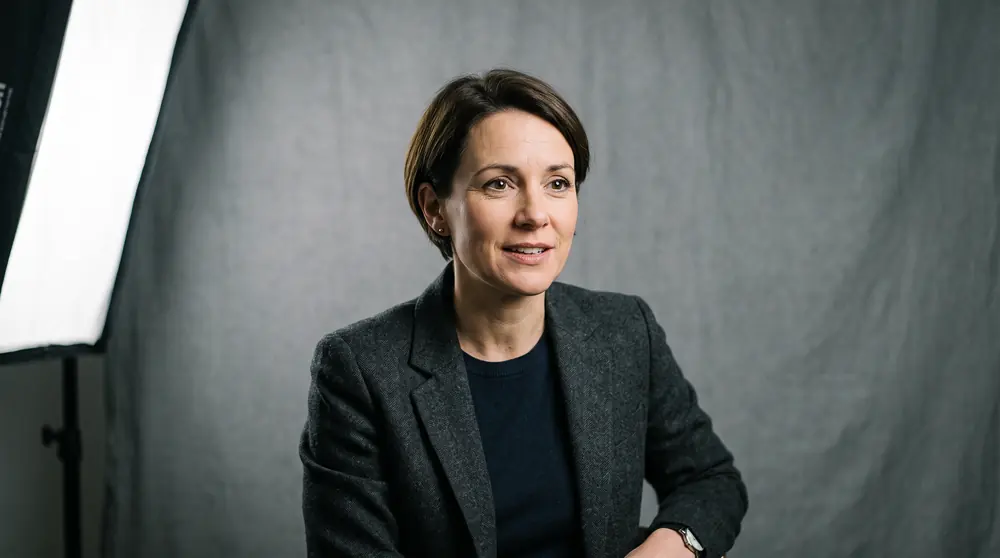 A close portrait of a presenter lit by a large softbox, a catchlight in each eye, plain grey backdrop behind